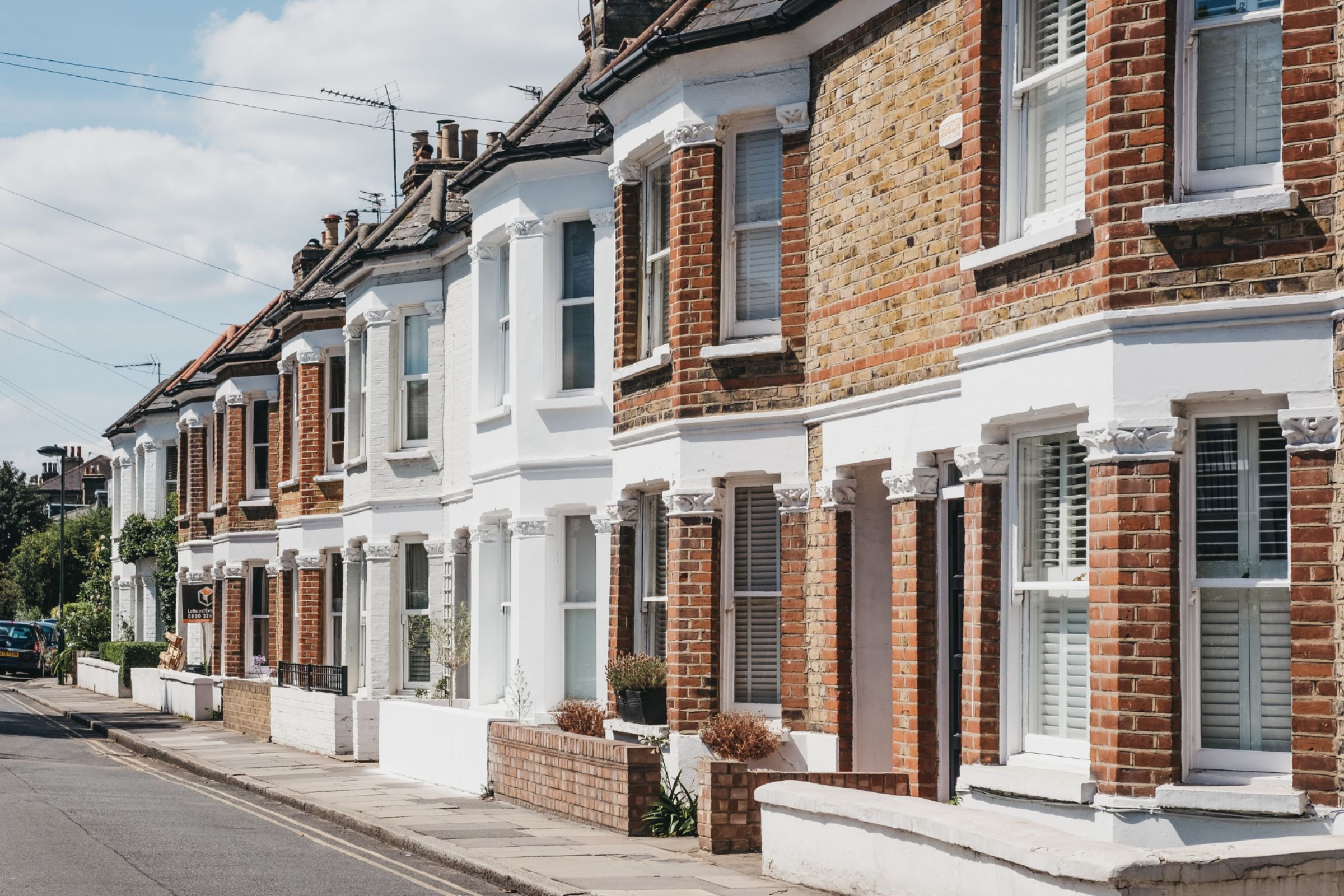 A row of traditional red-brick terraced homes on a sunlit street